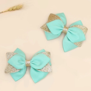 Close-up of mint green and gold glitter ribbon bow hair clips on a beige background