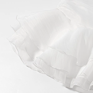 Dettaglio macro di balze bianche a strati su una gonna di chiffon leggera con finitura lucida