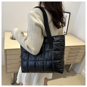 Quilted black down tote bag with square stitching and wide strap on model's shoulder
