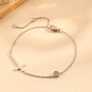 Minimalist silver titanium steel cross bracelet with a round zircon on beige leather background
