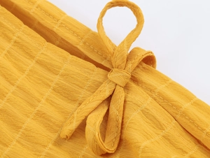 Dettaglio del tessuto giallo con coulisse e nodo sul miniabito a strati stile vacanza