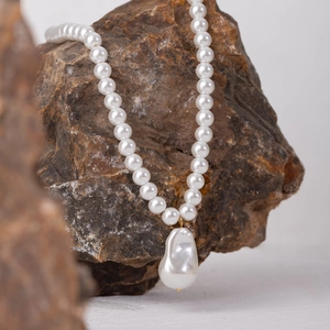 Collana con ciondolo a perla barocca con anello dorato su sfondo di roccia naturale