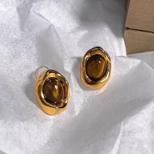 Detail view of golden irregular earrings with oval brown tiger eye stones on white paper