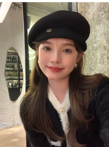 Detail of a chic black wool beret featuring a golden M letter pin on the side