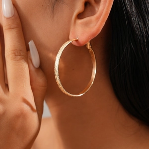 Detailed close-up of a large textured gold hoop earring worn by a model in a stylish pose