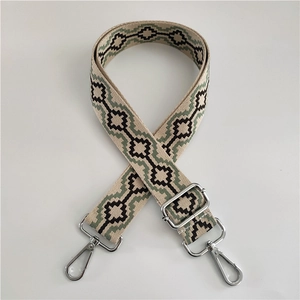 Detail view of woven shoulder strap with green geometric patterns and silver metal hooks