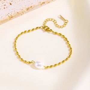 Detail of a gold beaded bracelet featuring a white pearl on a textured stone background