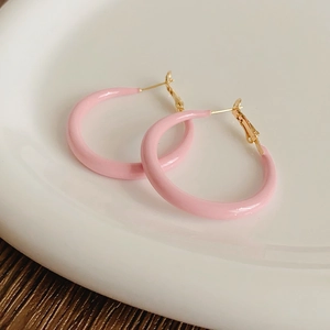 Close-up of large pink enamel hoop earrings with gold-plated pins on a white plate