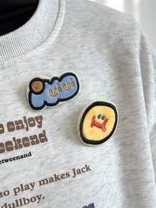 Grey crewneck sweatshirt featuring cartoon plush embroidery patches and graphic text