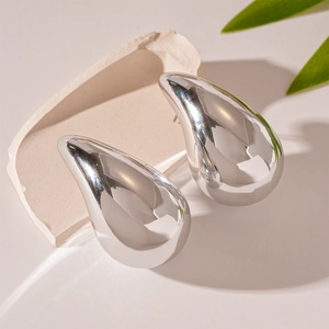 Polished silver teardrop earrings on minimalist stone and leaf display background