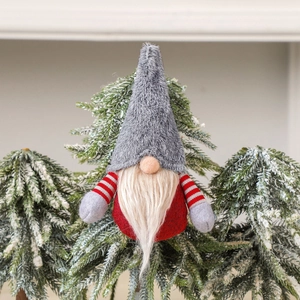 Charming grey and red Christmas gnome plush ornament hanging on a snowy pine branch