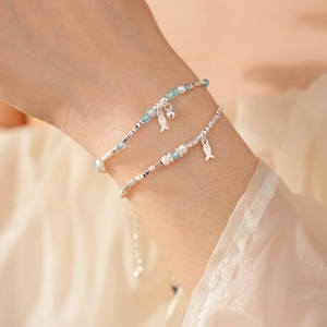 Close-up of layered silver pearl bracelet with blue beads and a fish charm on a wrist