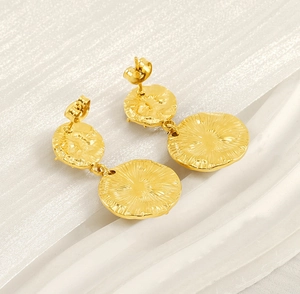 Détail de boucles d'oreilles doubles disques dorés avec textures radiales sur fond blanc