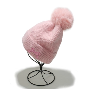 Detail of pink knitted hat featuring large faux fur pompom and embroidered bow decoration