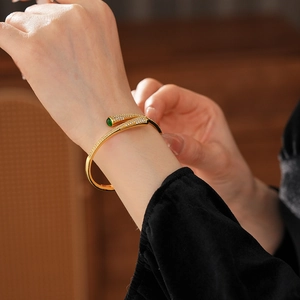 Detailed shot of a gold-plated open bangle with white zircon and a green teardrop gemstone