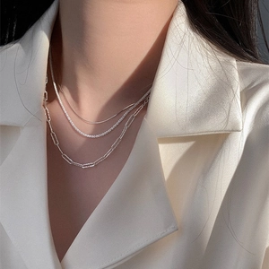 Detail of layered S925 sterling silver snake chain necklace on minimalist beige blazer