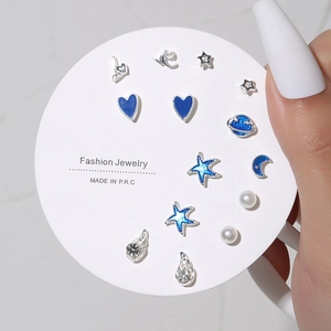 Close-up of 7 pairs of silver stud earrings with blue enamel stars and moons on a card