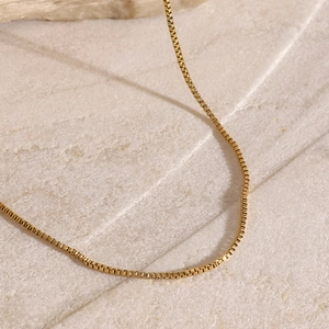 Close-up of golden box chain necklace with metallic luster on textured stone background