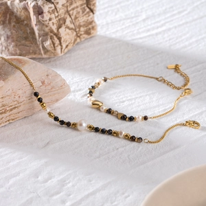 Golden chain bracelet with freshwater pearls and dark faceted beads on a stone surface