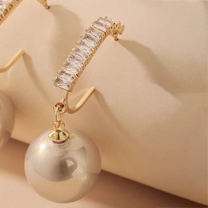 Macro shot of gold drop earrings featuring rectangular zircon stones and large pearls