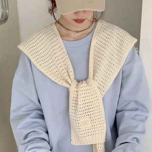 Detail of beige knit shawl with hollow mesh weave and decorative DD letter tag