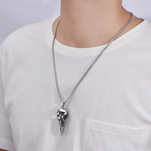 Detail view of a punk silver crow skull pendant necklace worn by a male model on a white tee