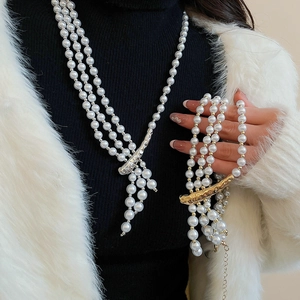 Detail of multilayer pearl necklace and bracelet with fluid metal accents on black knitwear