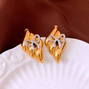 Detailed view of bicolor metal bow earrings with gold texture on a ceramic tray