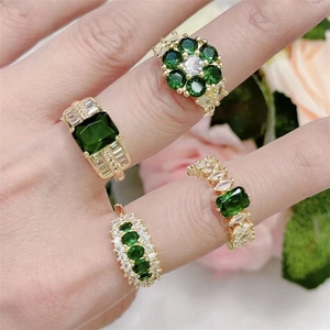 Close-up of four gold rings with green and clear zircon stones worn on hand