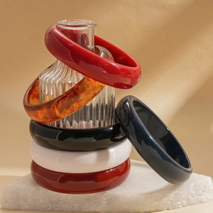 Stack of retro colorful resin geometric bangles displayed on a decorative glass vase