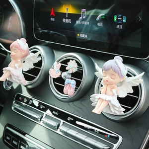 Detail view of cute resin angel car air vent clips with floral accessories on dashboard