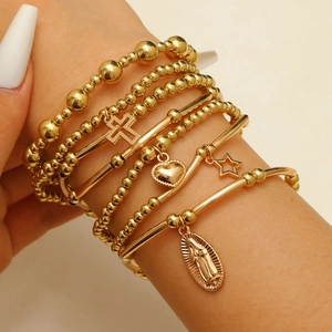 Detail view of a stacked gold bracelet set with cross and religious medal charms on model
