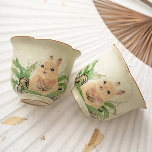 Celadon ceramic tea cup with rabbit motifs and petal shaped rim on white background