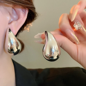 Detailed close-up of large polished silver water drop earrings worn on model's ear
