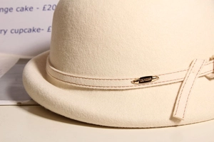 Detailed close-up of cream wool felt hat featuring brown stitching and a gold oval buckle