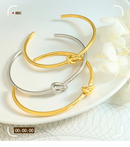 Detailed close-up of three minimalist knotted open bangles in gold and silver finish