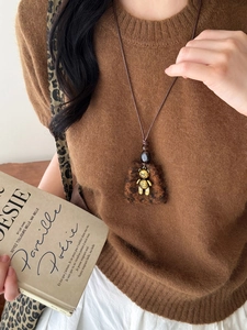 Macro view of plush brown bear pendant with golden metal details on vintage rope chain