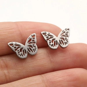 Macro view of silver butterfly wing earrings with detailed cutout patterns on a finger