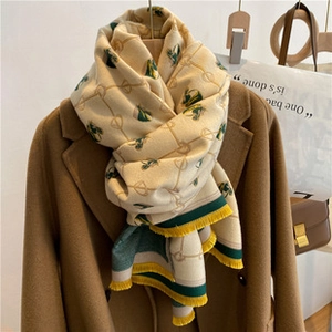 Detail view of beige cashmere feel scarf with green equestrian pattern and tassels on a coat