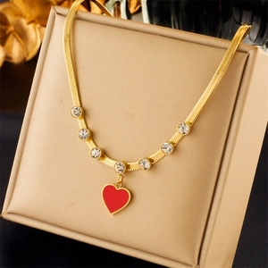 Detail of a gold snake chain necklace with a red heart pendant and crystals in a box