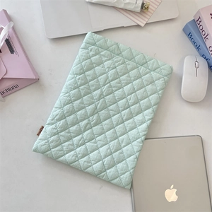 Close-up of light green quilted laptop sleeve with diamond stitching and side brand label