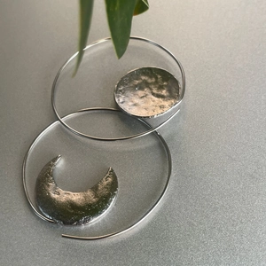 Detailed close-up of asymmetric silver moon and sun drop earrings with hammered texture finish