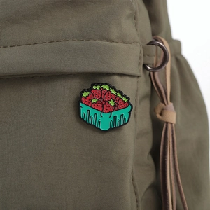 Gros plan détaillé d'un pin's panier de fraises en émail sur un sac en toile verte