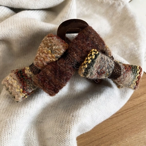 Detail view of a brown knit double-layered bow hair claw clip on a soft textured background