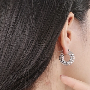 Gros plan de boucles d'oreilles rondes argentées avec motif ajouré portées par un mannequin