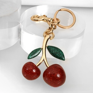 Close-up of glittery red cherry keychain with gold metal clasp and green leaves details