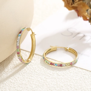 Chic gold hoop earrings with colorful crystals on a minimalist ceramic background