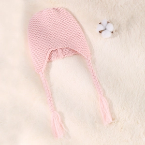 Detailed close-up of pink knit baby hat with braided tassels on soft white faux fur background