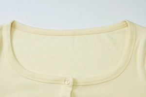 Detail of light yellow knit cardigan featuring a U-shaped neckline and a cream button