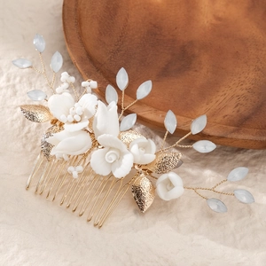 Elegant bridal hair comb with handmade white ceramic roses and gold leaves on wood